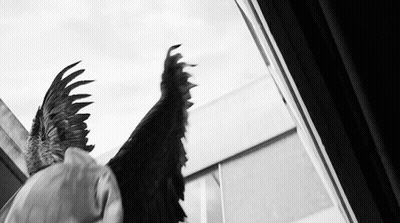 A Black And White Photo Of A Person With Wings Looking Out A Window GIF