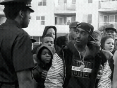 A Black And White Photo Of A Police Officer Talking To A Man In A Crowd . GIF