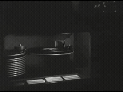 A Black And White Photo Of A Record Player And A Stack Of Records GIF