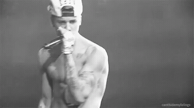 A Black And White Photo Of A Shirtless Man In A Baseball Cap Holding His Chest . GIF