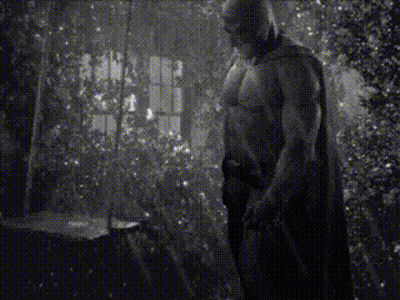 A Black And White Photo Of A Shirtless Man In A Cape Standing In A Room . GIF