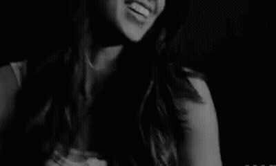 A Black And White Photo Of A Smiling Woman In A Dark Room . GIF