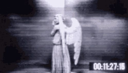 A Black And White Photo Of A Statue Of An Angel Holding A Light In A Dark Room . GIF