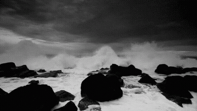 A Black And White Photo Of A Stormy Ocean With Waves Crashing Against Rocks . GIF