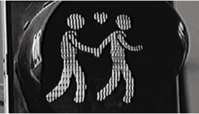 A Black And White Photo Of A Traffic Light With Two People Holding Hands GIF