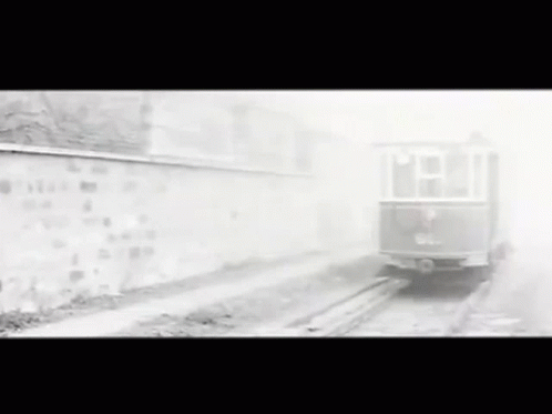 A Black And White Photo Of A Train Going Down The Tracks . GIF