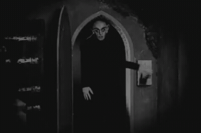 A Black And White Photo Of A Vampire Standing In An Archway . GIF