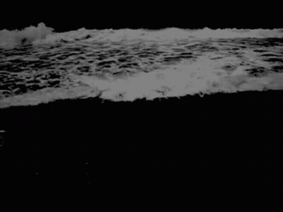 A Black And White Photo Of A Wave Crashing On A Beach . GIF