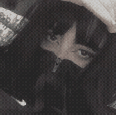 A Black And White Photo Of A Woman Covering Her Face With A Hood GIF