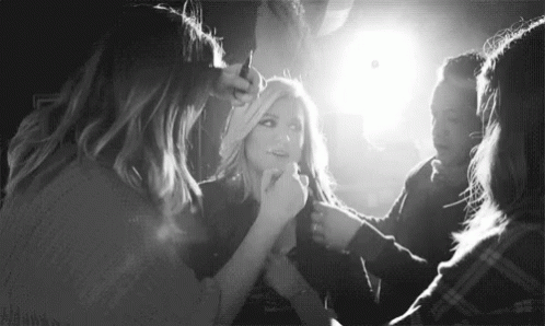 A Black And White Photo Of A Woman Getting Her Hair Done By A Group Of Women . GIF
