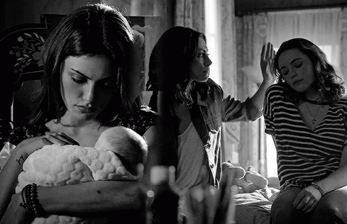 A Black And White Photo Of A Woman Holding A Baby And Another Woman Sitting On A Bed . GIF
