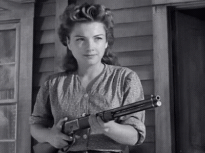 A Black And White Photo Of A Woman Holding A Shotgun . GIF