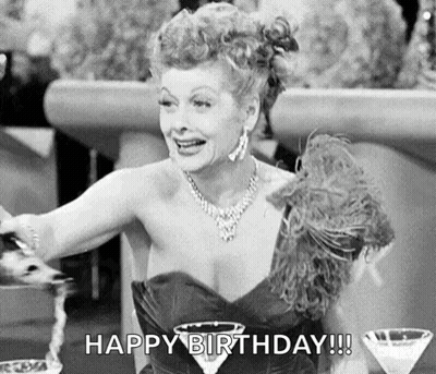 A Black And White Photo Of A Woman In A Dress Sitting At A Table With A Martini Glass And A Feather Boa . GIF