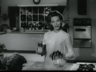 A Black And White Photo Of A Woman In A Kitchen Holding A Bottle GIF