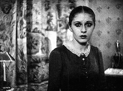 A Black And White Photo Of A Woman In A Room With A Lamp In The Background . GIF