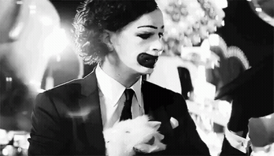 A Black And White Photo Of A Woman In A Suit And Tie With A Clown Makeup On Her Face . GIF