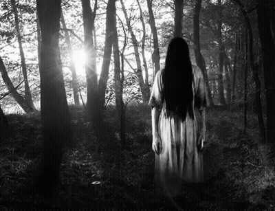 A Black And White Photo Of A Woman In A White Dress Standing In The Woods . GIF