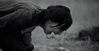 A Black And White Photo Of A Woman Kneeling Down With Her Head On A Dead Body . GIF