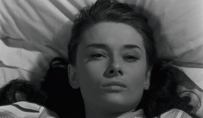 A Black And White Photo Of A Woman Laying In Bed Looking At The Camera . GIF