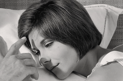 A Black And White Photo Of A Woman Laying In Bed With Her Hand On Her Forehead GIF