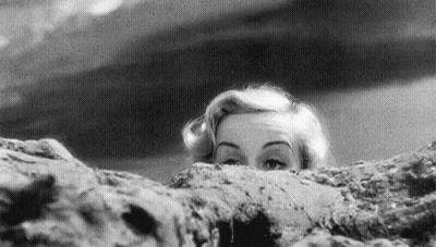 A Black And White Photo Of A Woman Peeking Over A Rock . GIF