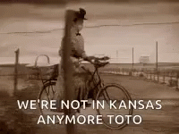 A Black And White Photo Of A Woman Riding A Bike With The Caption We 'Re Not In Kansas Anymore Toto . GIF
