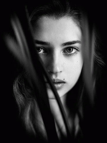 A Black And White Photo Of A Woman 'S Face Behind A Few Leaves GIF