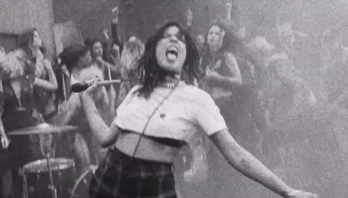 A Black And White Photo Of A Woman Singing Into A Microphone In Front Of A Crowd Of People . GIF