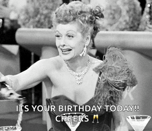 A Black And White Photo Of A Woman Sitting At A Table With A Martini And A Feather Boa . GIF
