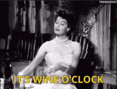 A Black And White Photo Of A Woman Sitting At A Table With The Words " It 'S Wine O ' Clock " GIF