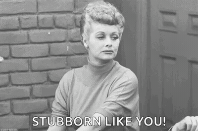 A Black And White Photo Of A Woman Sitting In Front Of A Brick Wall Saying `` Stubborn Like You '' . GIF
