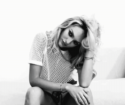 A Black And White Photo Of A Woman Sitting On A Couch Wearing A White Shirt . GIF