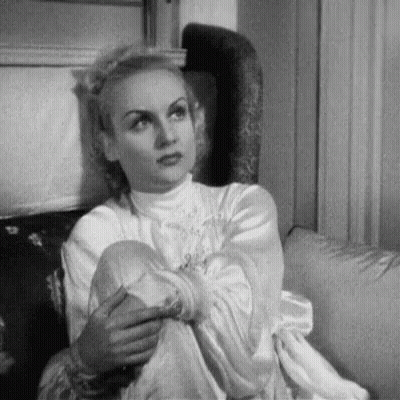 A Black And White Photo Of A Woman Sitting On A Couch With Her Legs Crossed . GIF