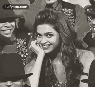 A Black And White Photo Of A Woman Smiling While Sitting In A Crowd Of People . GIF