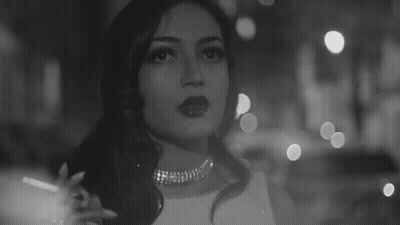 A Black And White Photo Of A Woman Smoking A Cigarette In A Dark Room . GIF
