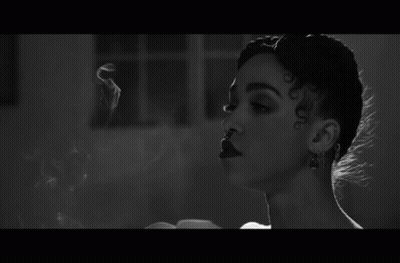 A Black And White Photo Of A Woman Smoking A Cigarette In A Room . GIF