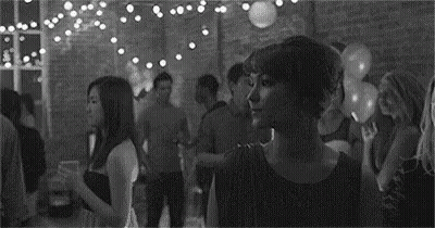 A Black And White Photo Of A Woman Standing In A Crowded Room At A Party . GIF