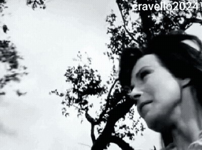 A Black And White Photo Of A Woman Standing In Front Of A Tree . GIF