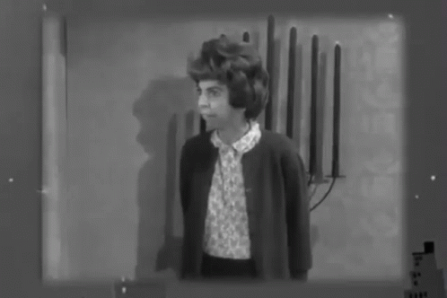 A Black And White Photo Of A Woman Standing In Front Of A Wall With Candles On It . GIF