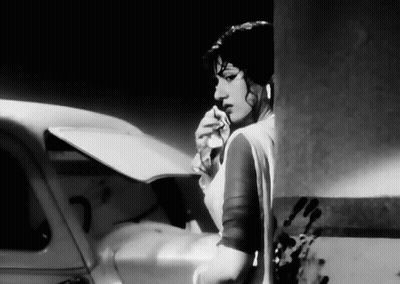 A Black And White Photo Of A Woman Standing Next To A Car Holding A Piece Of Paper . GIF