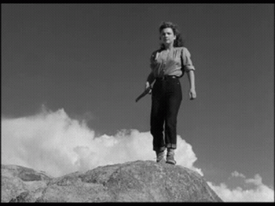 A Black And White Photo Of A Woman Standing On A Rock Holding A Knife . GIF