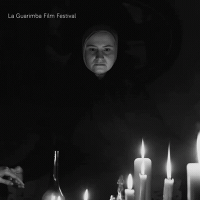 A Black And White Photo Of A Woman Surrounded By Lit Candles And The Words La Guarimba Film Festival Below Her GIF