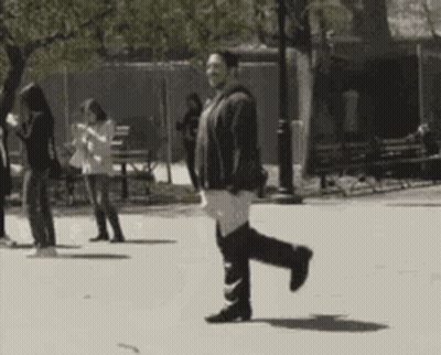 A Black And White Photo Of A Woman Walking Down A Street GIF