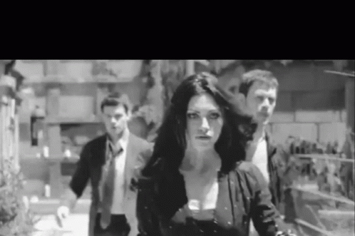 A Black And White Photo Of A Woman Walking With Two Men In Suits . GIF
