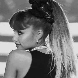 A Black And White Photo Of A Woman Wearing A Ponytail And Pearls GIF