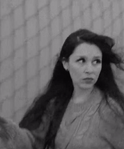 A Black And White Photo Of A Woman With Long Hair In Front Of A Fence . GIF