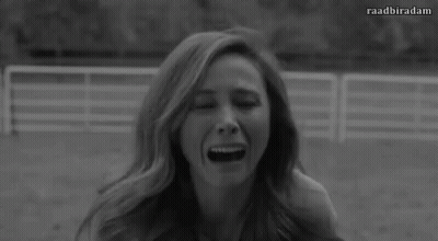 A Black And White Photo Of A Woman With Long Hair Sitting In A Field . GIF