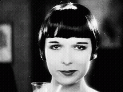 A Black And White Photo Of A Woman With Short Hair Looking At The Camera . GIF