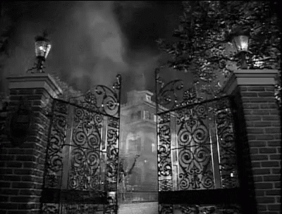 A Black And White Photo Of A Wrought Iron Gate Leading To A Mansion . GIF
