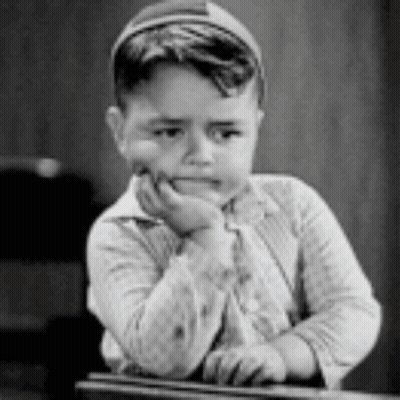 A Black And White Photo Of A Young Boy Sitting At A Desk With His Hand On His Chin . GIF